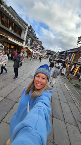 Reviewer takes a selfie wearing the blue marled pom beanie on a street.