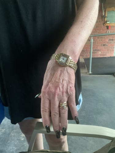 Customer wearing their classic, gold GREALY DE MAINS watch on their wrist, paired with a black top.