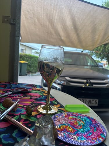 Reviewer's glass of Low Alcohol Sparkling wine in a gold-stemmed glass on a colorful outdoor table.