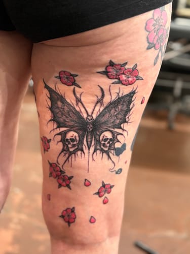 Customer shows their fresh thigh tattoo of a large butterfly with skulls after using The Painless All-Stars Kit for the session.
