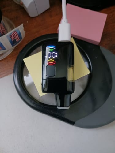 Reviewer's black Calm Vape plugged in and charging, showing its colorful lit-up digital display.