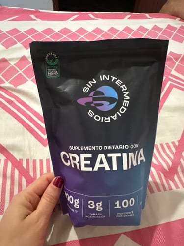 Un cliente sostiene el empaque del suplemento Creatina Monohidrato, mostrando la bolsa negra con detalles morados.