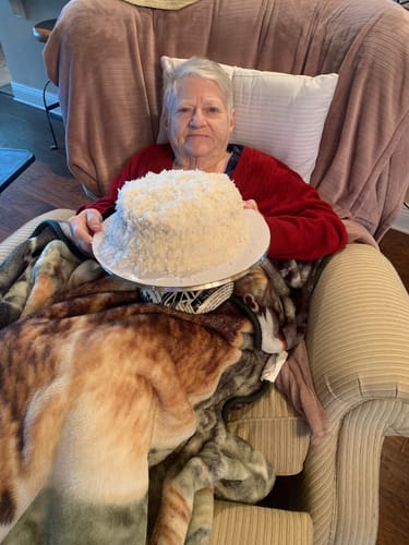 Customer's photo of an elderly woman sitting in a chair with a blanket, holding a white cake.