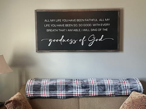 Reviewer's black Goodness Of God Faith Sign II hanging on a wall above a sofa.