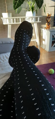 En kund visar sina svarta, mönstrade Diasocks stödstrumpor med fötterna i kors inomhus.