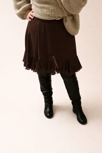 Kundin trägt den fließenden, braunen Rock "Summer" mit Volant-Saum, kombiniert mit Stiefeln und Pullover.