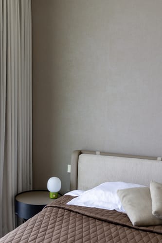 Customer's dark XO Bedside Table shown in a bedroom setting next to an upholstered bed.