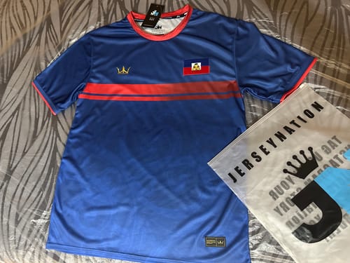 Customer's blue Haiti Heritage Football Jersey laid out flat, showing the red stripe and Haitian flag patch on the chest.