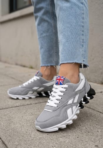 Reviewer wearing grey Ortho Step 2.0 shoes with white accents and a distinct black and white sole on a pavement.