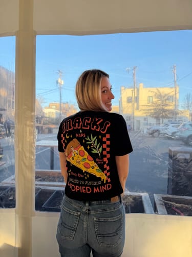 Reviewer smiling over their shoulder while wearing the black Snacks and Naps T-Shirt, showing the back graphic.