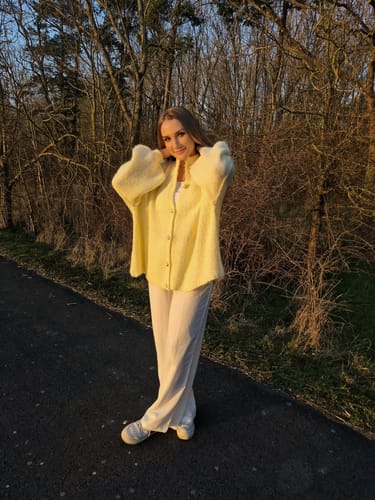 Kundin im wunderschönen gelben Oversized-Cardigan 'CozyGlam' bei einem Spaziergang im Freien.