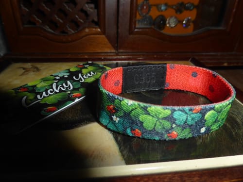 Customer's Lucky You Bracelet with a shamrock and ladybug pattern, shown next to its matching card on a wooden surface.