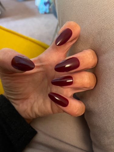 Customer's hand showing off the glossy, long Red Wine Press On Nails in an almond shape.