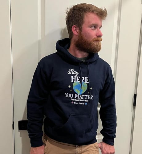 Reviewer wearing the dark Smile | Stay Here Hoodie, showing the 'Stay Here You Matter' graphic on the chest.