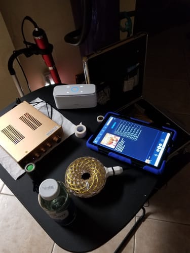 Reviewer's Qi Coil Max Transformation System set up on a table with the golden console, one coil, and a tablet running the app.