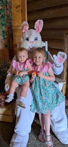 Customer's two children in matching turquoise floral outfits, a dress and a bloomer set, sitting with a large bunny mascot.