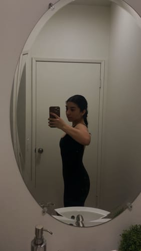 Reviewer showing the form-fitting side view of the black Curve Onesie in a mirror selfie.