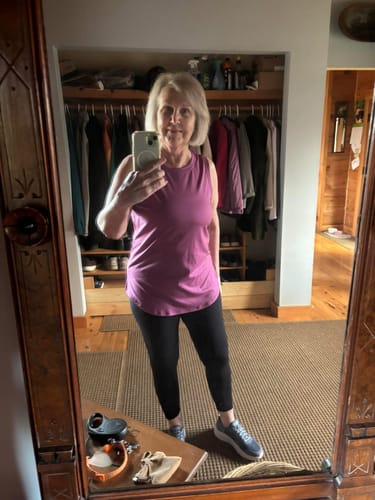 Reviewer in a mirror selfie wearing the purple Bella Tunic Top with black leggings.