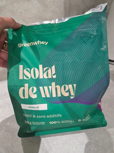 Un client tenant le sachet vert d'Isolat de Whey Native, saveur vanille, dans sa main.
