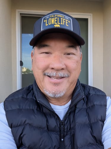 Reviewer smiling while wearing a dark California 60's Plate Hat customized with the text 'LOWELIFE'.