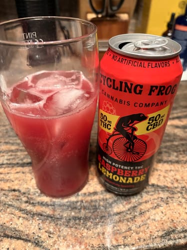 Customer's can of Sparkling THC Raspberry Lemonade next to a glass of the red beverage poured over ice.