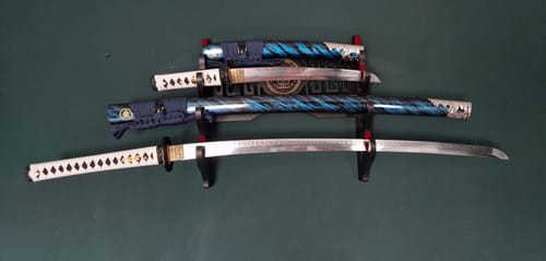 Customer's Katana & Wakizashi set displayed on a wall rack with blades unsheathed next to their blue patterned scabbards.