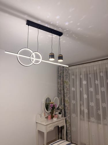Recenzent arată lustra LED suspendată modernă, aprinsă într-un dormitor, proiectând steluțe pe tavan.
