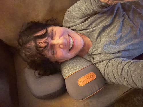 Reviewer smiling while using the grey Original Callixe Thera Back Pillow on a couch.