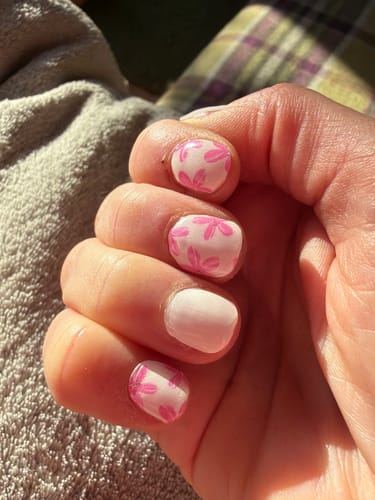 Close-up of a customer's hand with Essentials gel nails, featuring a pink floral design and a solid accent nail.