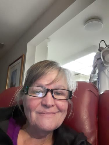 A smiling reviewer for the Qi Coil™ Mini System sitting in a red chair.