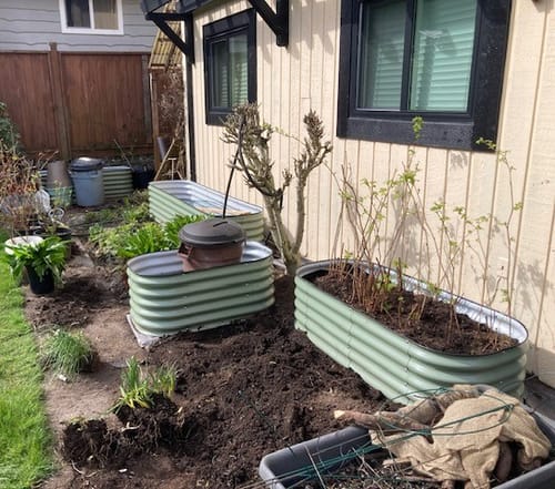 Customer's installation of several tall, green raised garden beds of various sizes in a backyard.