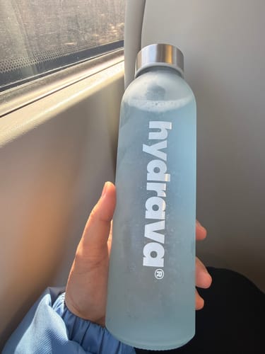 Reviewer's hand holding a frosted light blue bottle of their Hydrava electrolyte drink while on the go.