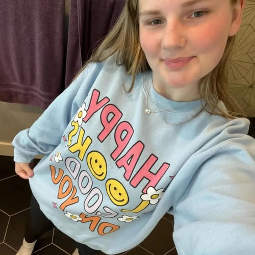 Reviewer takes a selfie while wearing the light blue 'Happy Looks Good On You Crewneck'.