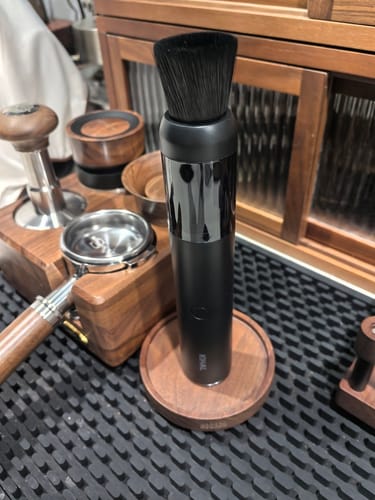 Reviewer's black Barista Air Wand with a brush attachment, standing on a wooden base among coffee accessories.