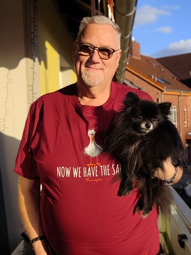 Kunde trägt das rote „Now we have the Salad“ T-Shirt und hält einen kleinen schwarzen Hund auf dem Arm.