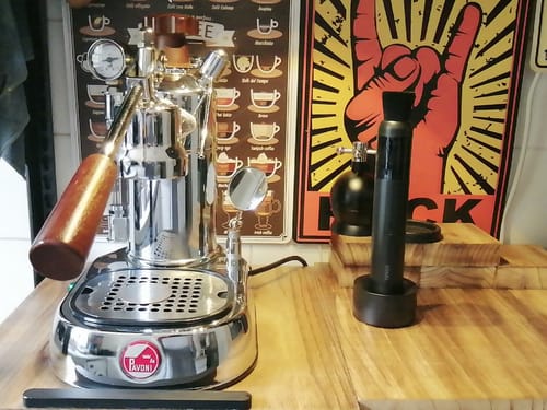 Customer's black Barista Air Wand in its stand on a wooden counter next to a chrome espresso machine.