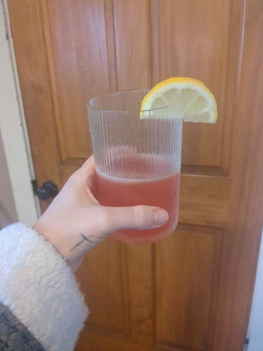 Customer holding a ribbed glass of pink Migranium Daily, garnished with a fresh lemon slice.