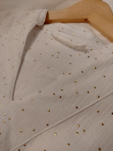 Gros plan par une cliente sur le col en V et le tissu blanc à pois dorés de la blouse Isabeau.