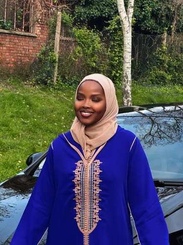 Close-up of a reviewer smiling outdoors in the vibrant blue Jellaba Sphene, showing its intricate embroidery.