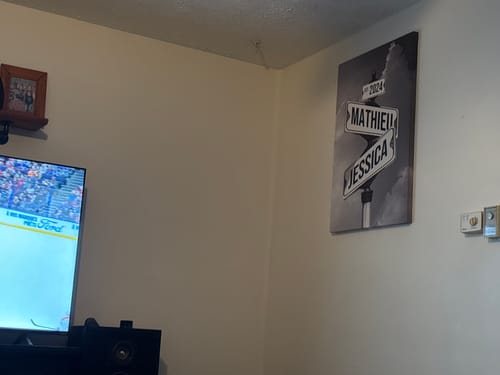 Customer's personalized canvas with street signs for 'Mathieu' and 'Jessica' and the year 2024, hung on a living room wall.