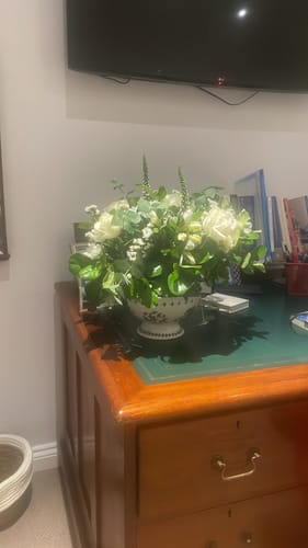 Customer's beautiful Tranquility Flower Arrangement with white flowers and greenery in an ornate vase on a desk.
