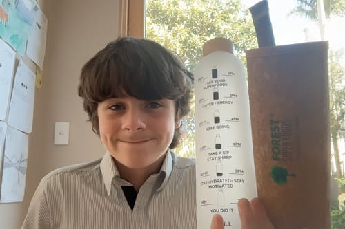 Reviewer holds the Borosilicate Glass Drinking Bottle showing its time markers, with the brown case visible.