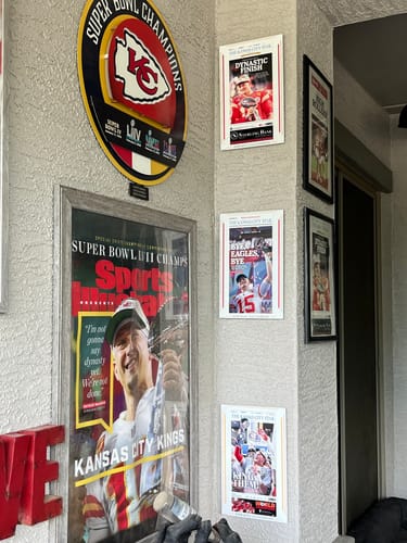 Reviewer's Kansas City Chiefs Super Bowl front page print displayed on a wall with other team memorabilia.