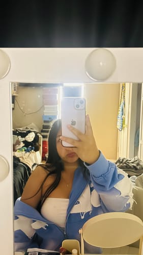 Reviewer in a mirror selfie wearing the blue and white patterned SEEK ZIPUP, partially unzipped.