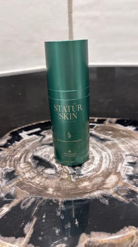 Customer's Elite Essence Soothing Elixir, from the Restoration Ritual Set, in a green bottle on a marbled counter.