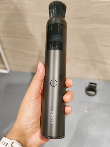A customer's hand holding the Barista Air Wand, a sleek, dark grey vacuum with a brush attachment.