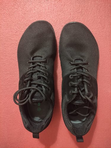 Draufsicht auf die schwarzen, geschnürten Wish Ⅰ Barfußschuhe eines Kunden auf einer roten Oberfläche.