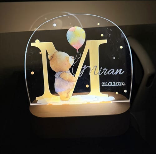 Rezensent zeigt das leuchtende personalisierte Nachtlicht mit Bärenmotiv, dem Initial M und dem Namen Miran auf seinem Holzsockel.
