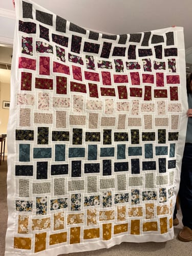Customer holding up their completed Dream Weaving Quilt, showing colorful patterned blocks arranged in rows.