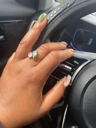 Reviewer's hand on a steering wheel, wearing a gold ring with a toi et moi design.